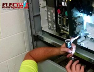 Technician tightening a component inside an electrical panel; Electric Power Systems logo visible in the corner.